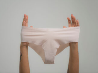 Gros plan de mains tenant des sous-vêtements blancs contre un arrière-plan subtil