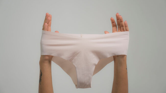 Gros plan de mains tenant des sous-vêtements blancs contre un arrière-plan subtil